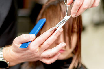 Hands of hairdresser cutting hair tips of woman in beauty salon.