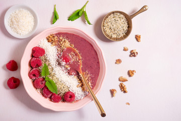 Overhead view of a berry smoothie bowl with ingredients on a pink surface with copy space