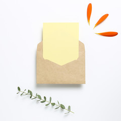 Kraft envelope and empty card with flower leaves, eucalyptus leaves on white background. Floral composition, flat lay, top view, copy space