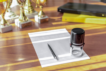 Workplace office space with a blank sheet, pen, stamp, folders and trophies on a blurred background. Sport business concept. Selective focus.
