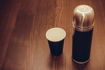 The thermos and coffee Cup are on the table. Brown tinting
