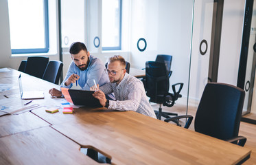 Concentrated male colleagues 20s watching online media content analyzing information from social...