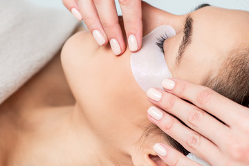 Cosmetologist hand putting strip under woman eye before eyelash extension procedure.