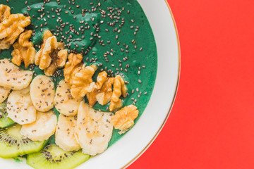 spirulina smoothie bowl with banana, walnuts, kiwi and chia seeds on red background