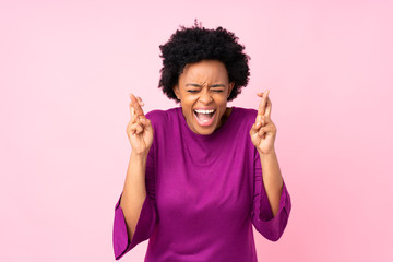 African american woman over isolated pink background with fingers crossing