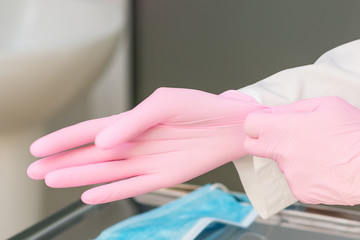 Nurse hands puts on pink gloves in hospital close up.