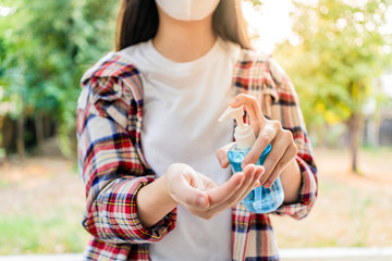 Obraz premium Young woman using anti-septic alcohol hand gel to clean her hands, blurred trees and garden background