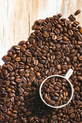 Roasted coffee beans with cup and wood background