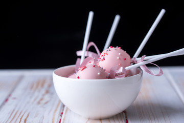 Delicious dessert cake pops in pink milk chocolate in white piala on a wooden background.