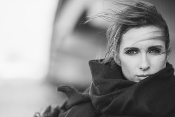 Beautiful lonely woman in a coat and scarf with her hair developing in the wind under a bridge on a...