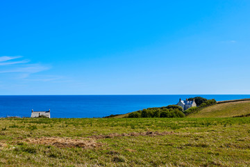 Fototapeta na wymiar View across the Cornish Headland with grass and a house in the foreground and the English Channel in the background with a blue sky. Cornwall, England UK