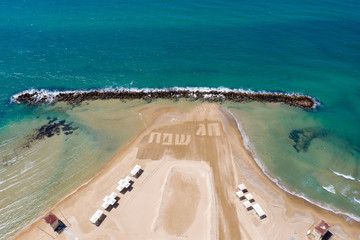 Happy Holiday in Hebrew letters written in Sand on a beach, Aerial view.
