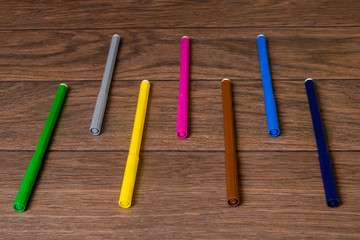 A lot of multi-colored colorful vibrant felt-tip pens on a brown wooden background.