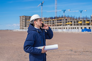 a civil engineer in a white helmet is talking on the phone in the background of construction.