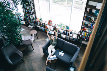 Happy student with laptop and textbook in library