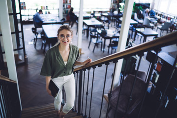 Smiling student with books on stairs in library