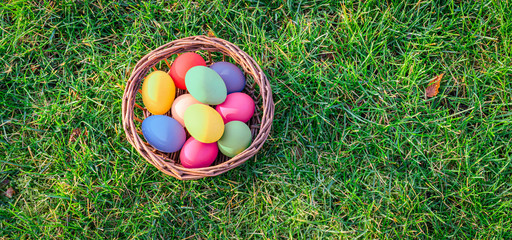 Overhead view of colorful easter eggs in basket on the grass.