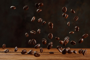 Flying roasted brown coffee beans flying on wooden background. Selective focus
