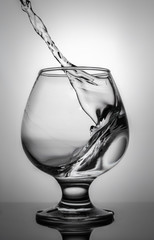 In a glass pour the liquid at an angle. Beautiful glass with a wave on a white background