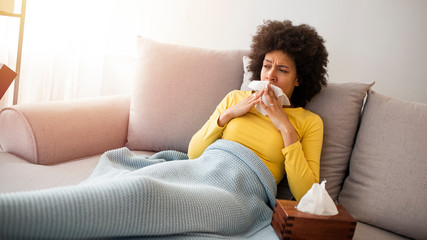 It's the season of sneezes. Sick desperate woman has flu. Rhinitis, cold, sickness, allergy concept. Pretty sick woman has runnning nose, rubs nose with handkerchief. Sneezing female.