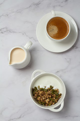 granola with seeds and yogurt in a white cup and black coffee with milk top view
