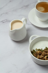 granola with seeds and yogurt in a white cup and black coffee with milk close-up
