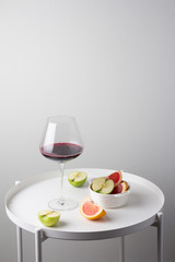a glass of red wine and fruit on the kitchen table against a white wall

