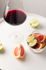 glass of red wine and fruits on a white table close-up
