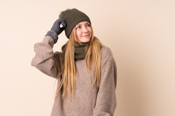 Teenager Ukrainian girl with winter hat isolated on beige background having doubts and with confuse face expression