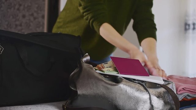 Young woman puts her belongings into a black travel bag. 