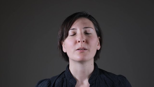 Portrait of a positive Caucasian woman breathing on a gray background