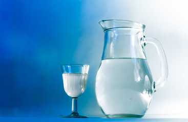 Glass jug of fresh milk on blue background
