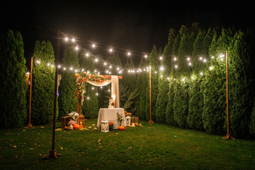 night wedding ceremony, the arch is decorated with flowers, candles and garlands of light bulbs and...
