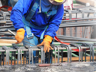 workers hands using steel wire and pincers to secure rebar before concrete is poured over it