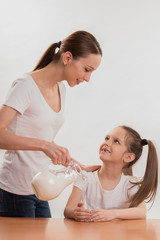 Obraz na płótnie Canvas Mom pours daughter a milk in a glass on a white background