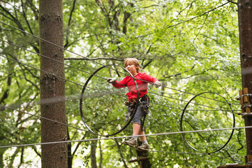 Little boy in forest adventure park walking high on rope, summer activities for children