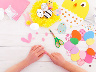Child makes craft gift his own hands at Easter. Pink easter bunny with flowers, step by step. Scissors, cardboard, eggs, chicken, rabbit, nest. DIY art creativity on wooden table. Top view, copy space