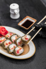 fried warm sushi with red caviar of fish rice wasabi ginger green on a black wooden background