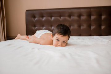 Cute toddler boy in diapers lies on bed with white sheet