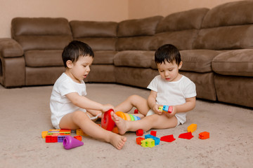 Two baby twin boys sit on the floor of the house and play educational games.Child playing with...