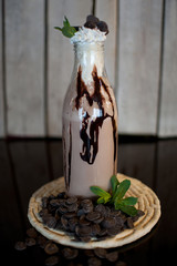 milkshake with chocolate and cream, decorated with chocolate topping on a wooden background in a glass bottle