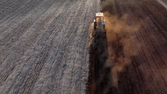 Tractor with seeder planting seeds of organic grain crops, fertilizes soil before planting, plowing land in rural field. Spring agricultural work at sunset. Aerial view. Top View.