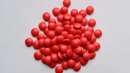 A scattered pile of red round frosted pills on a white background