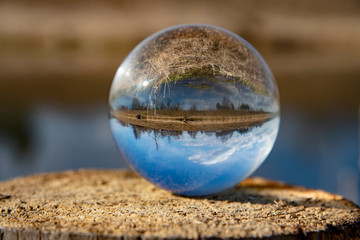Inverted image of the river and its banks in a glass ball standing on a stump. Selective focus.