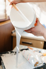 Paint roller with a brush paints the shelves and walls pours and flows with white paint