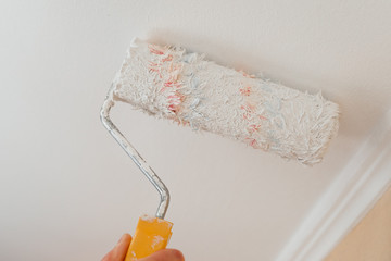 Paint roller with a brush paints the shelves and walls pours and flows with white paint