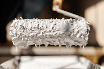 Paint roller with a brush paints the shelves and walls pours and flows with white paint