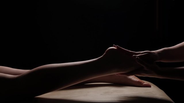 Massage of female legs, feet closeup on a black background. Slow motion. Thai massage.