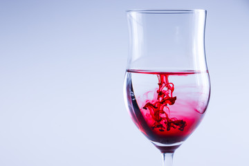 Red ink splash in water. Wine glass isolated.