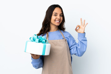 Pastry chef holding a big cake over isolated white background showing ok sign with fingers